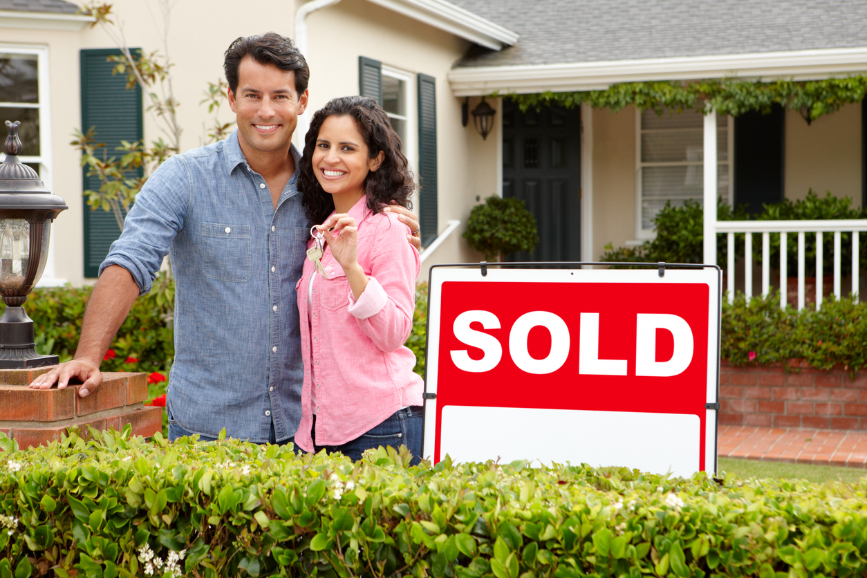 Hispanic couple outside home with sold sign. Relocating and need to sell house fast